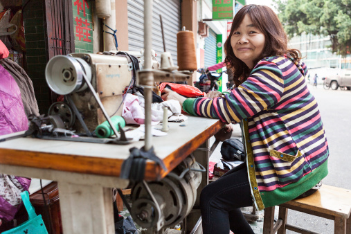 Shunde district of Foshan City, Guangdong Province, China aa March 16 2013: Unidentified seamstress provides her sewing services at a streetside shop in the Shunde District of Foshan City, Guangdong Province in Southern China.