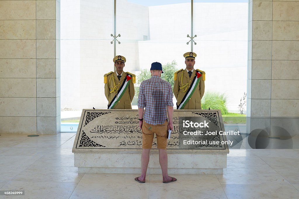 Tourist visiting Yasser Arafat's grave in Ramallah, Palestine Ramallah, West Bank, Palestinian Territories - July 23, 2013: A British visitor to the West Bank city of Ramallah, holding a guidebook and with a sweaty back from the summer heat, looks at the tomb of Yasser Arafat at the Palestinian Authority Presidential compound in Ramallah. Arafat was for decades the symbol of the Palestinian national movement. He died in 2004 while President of the Palestinian Authority. Two guards also stand over the tomb. Adult Stock Photo