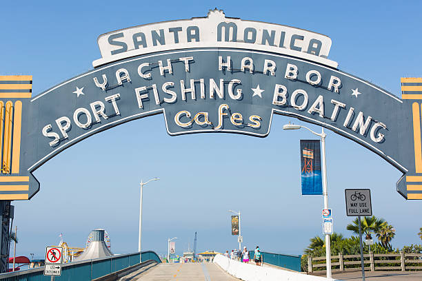 Santa Monica, California, USA - May 11, 2013: Tourists walk over the bridge leading to the pier from the famous Santa Monica Pier sign at the end of America's Route 66.