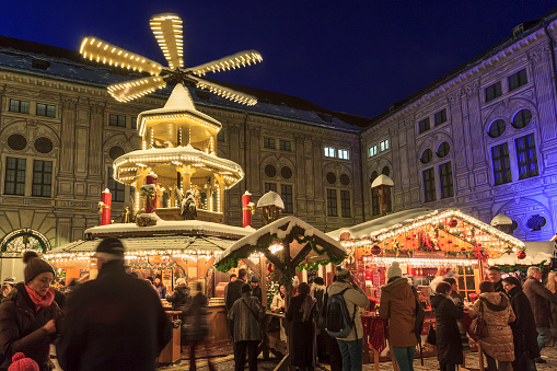Munich, Germany - December 12, 2012: People strolling in the Kaiserhof courtyard, part of the Residenz of Munich, where every year a very popular Christkindlmarkt is held. The stalls offer traditional German food and drink, as well as items and Christmas decorations. In the center of the square stands a large Saulenpyramide, a pyramid that turns as a carousel, a typical German handicraft product.
