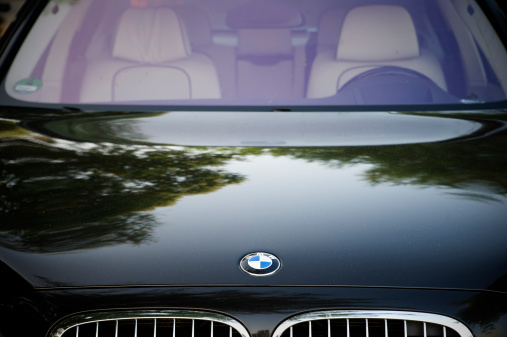 Padua, Italy - July 8, 2012: Circle shape BMW logo and part of the front grill and hood on a black Serie 7 BMW car. BMW (Bayerische Motoren Werke) is a German automobile, motorcycle and engine manufacturing company founded in 1916. Shot in a public parking.
