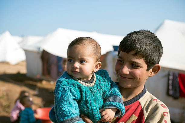 Atmeh, Syria - January 14, 2013: Syrian children take advantage of a mild winter day after days of frigid cold to be outside their tents at a displaced persons camp housing approximately 11,000 people. In addition to the two kids in the foreground, three other children are in the background around a tub for washing dishes.