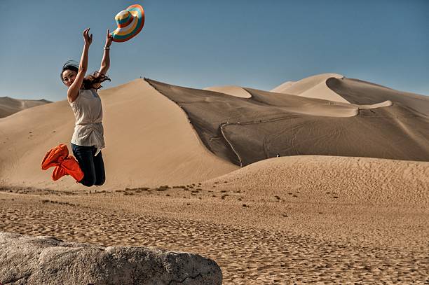 Dunhuang, Gansu province, China - June 29, 2012: Young Chinese woman taking a leap of joy at famous Mingsha sand dunes in the Gobi desert on the Silk road.