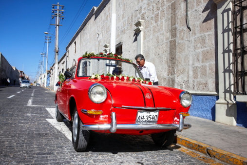 Arequipa, Peru - May 25, 2013: Peruvian man preparing red  vintage Volkswagen car for wedding by arranging garlands of flowers around the windshield