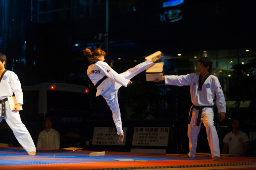 Seoul, Korea - September 17, 2009: An unidentified taekwondo girl in mid-air jump kicks and breaks a wood board at a free open-air summer show near city hall on September 17, 2009 in Seoul, Korea