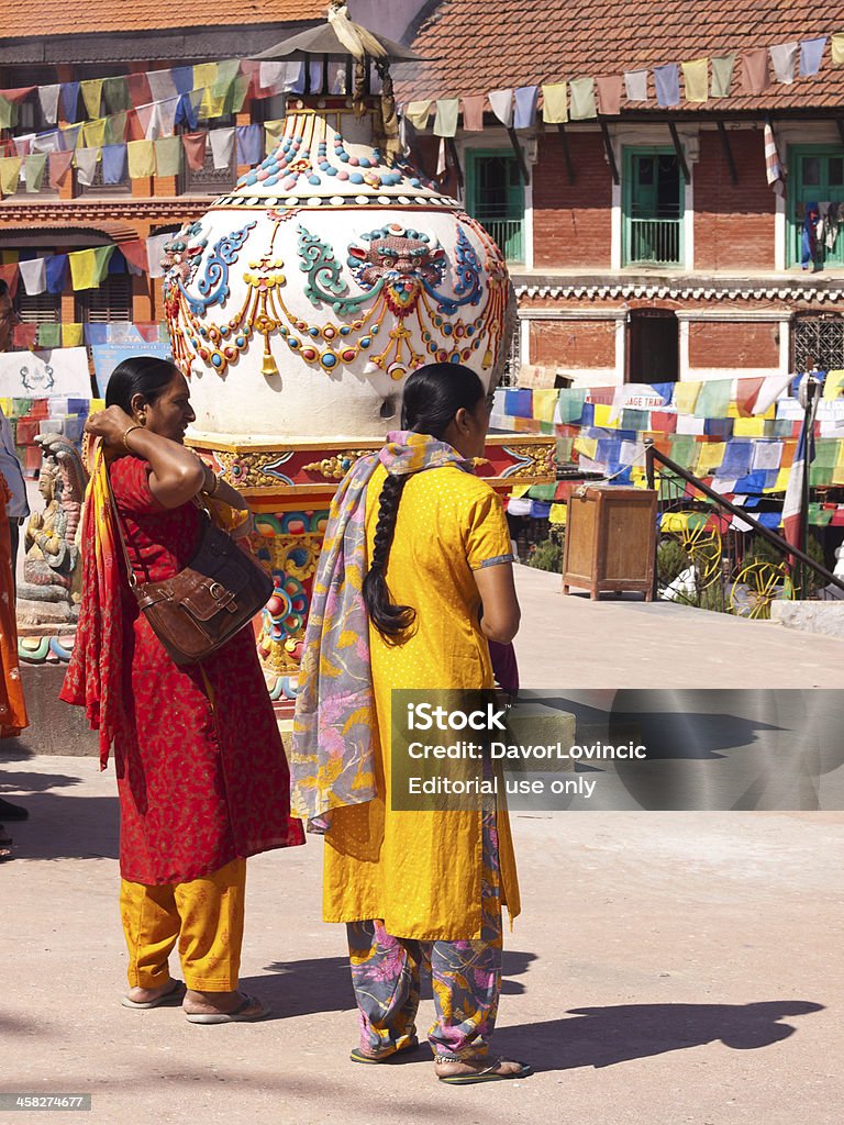 At Boudnanath Stupa Kathmandu, Nepal - October 16, 2009:Two women in traditional clothes are standing on Boudnanath pagoda and are getting ready for praying. Around are hanging praying flags and in background are surrounding houses. Adult Stock Photo