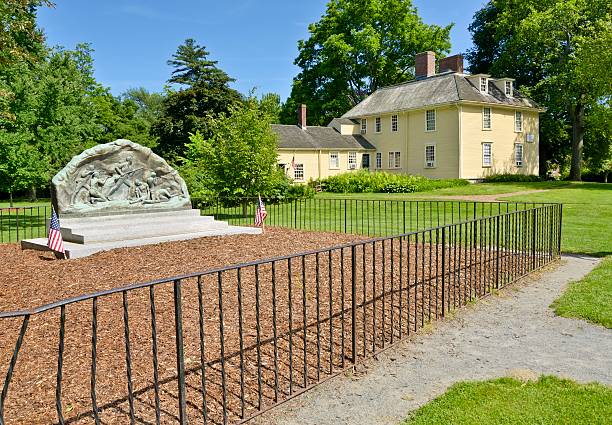 Lexington, Massachusetts, USA - June 10, 2012: A person at the historic Buckman Tavern in Lexington, Massachusetts. Founded about 1709, it hosted members of the militia at the dawn of the American Revolution. In the foreground, the Minute Men Memorial.