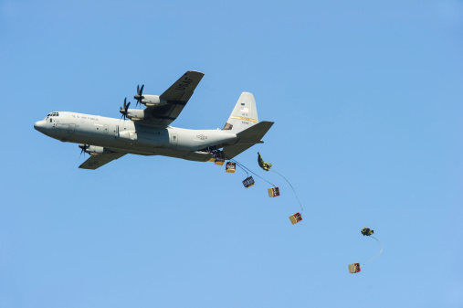 Jacksonville, Arkansas, USA - September 9, 2012: An air Force c-130 cargo plane makes a material drop out of the back door of the aircraft. The pilot angles the plane upward for gravity to allow the cargo to fall out and parachutes lower it to the ground.