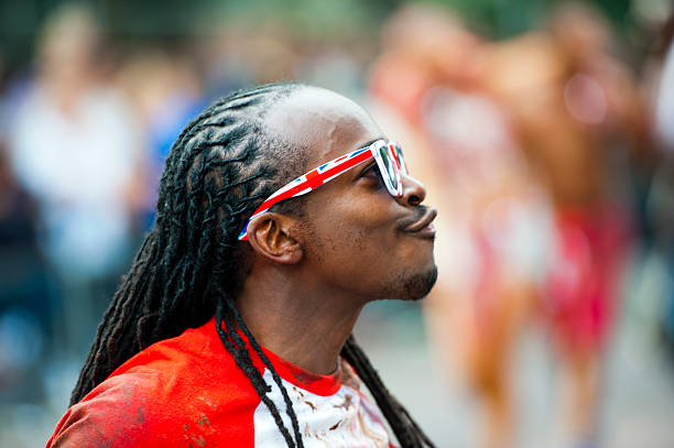 Young black man with sunglasses and headphones standing against blue background.