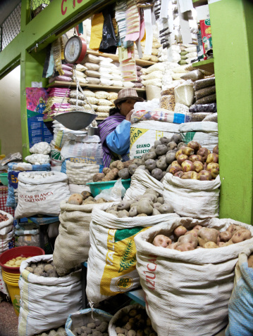 Puno, Peru - May 27, 2013: Female shopkeeper selling potatoes in Peruvian market. She is standing surrounded by various sacks of potatoes