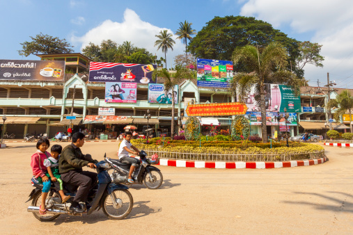 Tachileik, Myanmar - December 13, 2011: People ride on scooters near a roundabout in the town of Tachileik on the border between Myanmar and Thailand. The town is a popular destination for travellers making a visa run from Thailand, and Thai people looking for cheap goods from Myanmar.