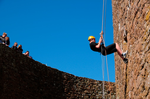 Jersey, U.K. - April 15, 2013: A teenager abseils down a medieval wall with his friends watching opposite at Mont Orgueil Castle, Grouville, Jersey. A persute open to all visitors if you dare.