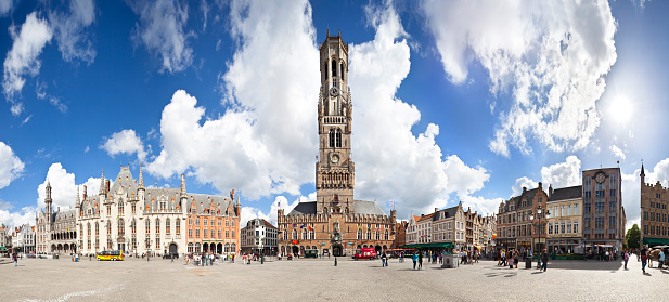 Bruges, Belgium - June 8, 2011: The Provincial Court and Belfry with some restaurants at the market square of Bruges at day, some tourists and locals in the background.