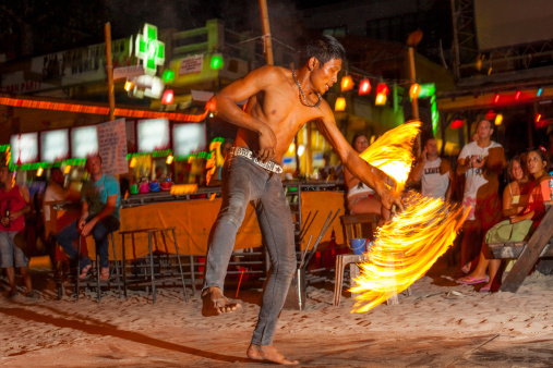 Surat Thani, Thailand - October 3, 2011: Adult fire twirler on the beach at Koh Phangan in Thailand. Image shows a view of the man and the motion blur of the fire. Image captured from the public beach at nighttime. A crowd of people can be seen in the background.