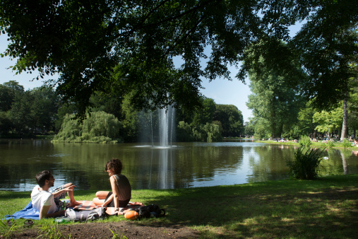 Utrecht, the netherlands - July 7th, 2013 : young couple relaxing in the grass in Utrechts wilhelminapark, the lake and fountain in the background