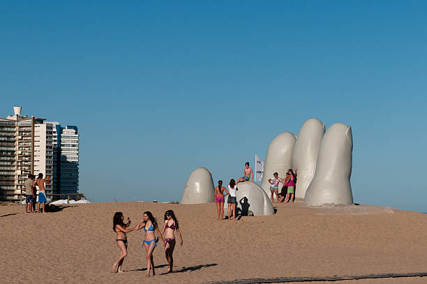 Monument to the Drowned, Punta del Este (Uruguay) Punta del Este, Uruguay - December 25, 2010: People posing for photographs near the Monumento al Ahogado, sculpture of five human fingers partially emerging from sand, located on Brava Beach, Punta del Este (Uruguay) playas del este stock pictures, royalty-free photos & images