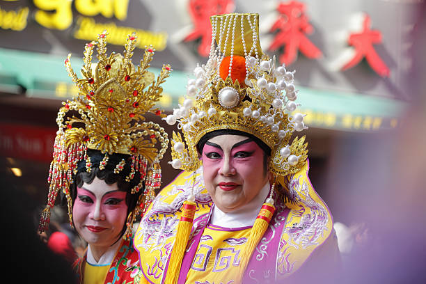 New York, NY, USA - February 17, 2013: Two Chinese actors dressed in traditional costume adorned with jewellery wait for the Lunar New Year parade to start on Mott Street in Manhattan's Chinatown. In the background is a sign for a restaurant.