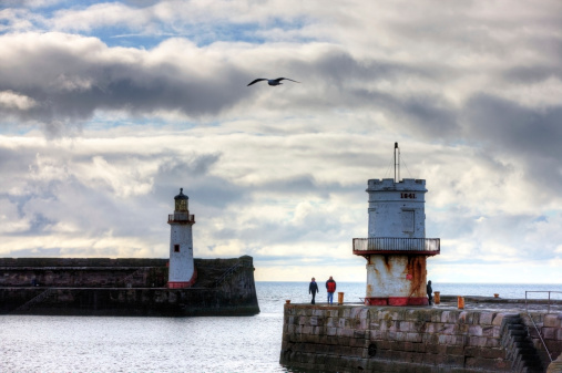 Whitehaven, England - March 17, 2013: Old lighthouse on Cumbria coastal town of Whitehaven. A couple are pictured walking around the circular building while a man fishing leans up against it