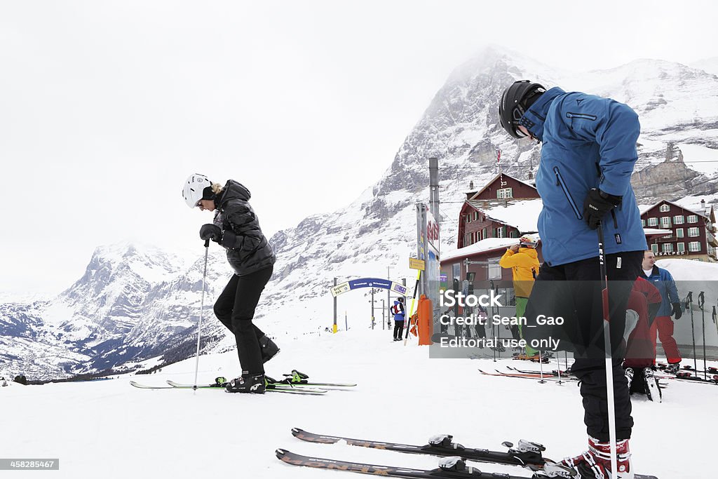 Skiers getting ready in Alps Kleine Scheidegg, Switzerland aa March 20, 2013: Skiers getting ready for a downhill ski in Kleine Scheidegg, Switzerland on March 20, 2013. On the foot of Jungfrau, Interlaken area attracts skiers and tourists alike around the globe. Alpine peaks, Eiger and Schreckhorn, are in the background. Crash Helmet Stock Photo