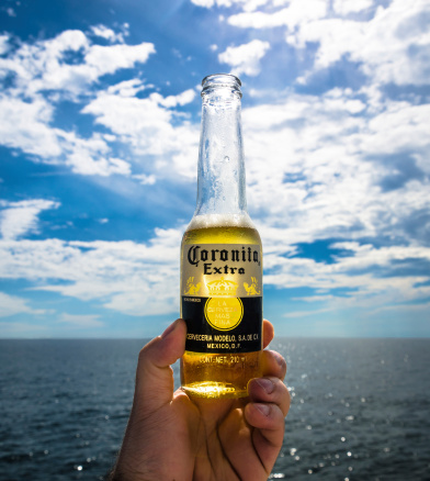 Acapulco, Mexico - May 4, 2013: A 220ml bottle of Coronita Extra beer in a summer sunny day, during a recreational sailing day in the ocean.Corona Extra is the leading brand in Mexico, the number one imported beer in the US, the fourth most valuable brand in the world and the most popular Mexican beer worldwide. It is a pilsner beer. The Corona Extra brand is targeted to people who are looking to relax responsibly. It is the only brand that stands for Mexican pride all over the world. It is currently sold in more than 170 countries in five continents and it is the leading import beer in almost fifty of such countries.Corona Extra was first produced in 1925 at the CervecerA-a Modelo in Mexico City.