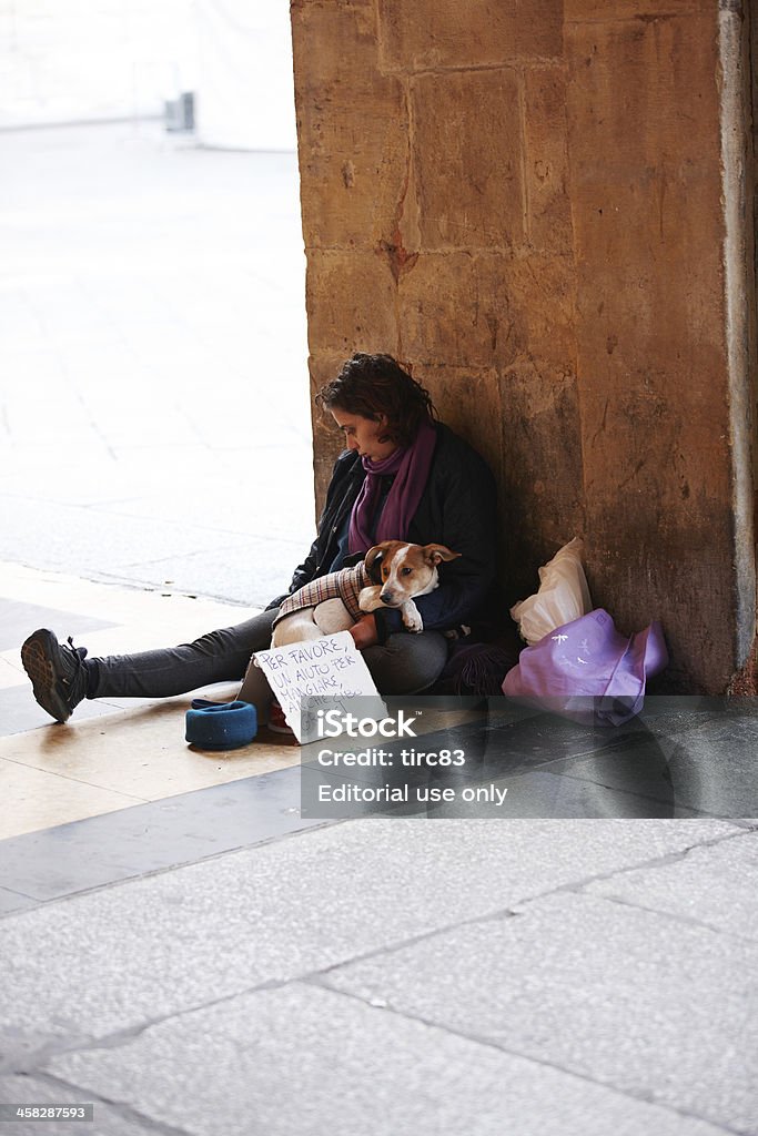 Young adult woman begging in italian city Bologna, Italy - November 8, 2012: Young adult woman sitting on stone floor reading a book and begging in the italian city of Bologna. She has a sign written in italian and has her pet dog sitting in her lap Adult Stock Photo