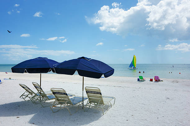 Beach scene on Marco Island Marco Island, Florida, USA - July 7, 2013: Marco Island beach scene with beach lounge chairs and sun umbrellas. People can be seen in the water and a Hobie catamaran sailboat is sailing just offshore. A brilliant cloudscape partially fills the blue sky and the Gulf of Mexico can be seen along the horizon. Marco Island is a popular vacation destination on the west coast of Florida. marco island stock pictures, royalty-free photos & images