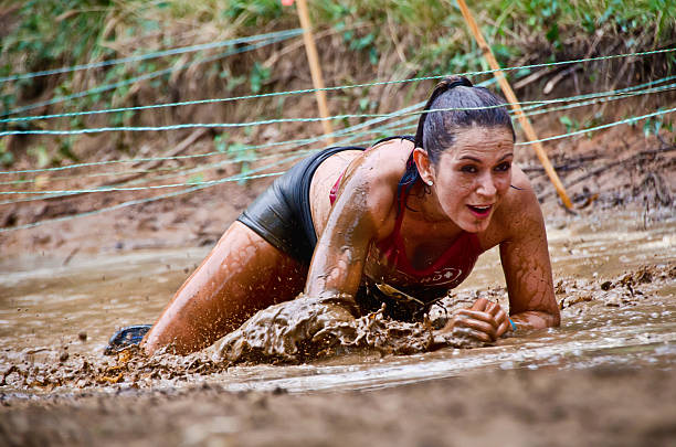 corrida na lama participante gatinhar sob os fios - mud run imagens e fotografias de stock