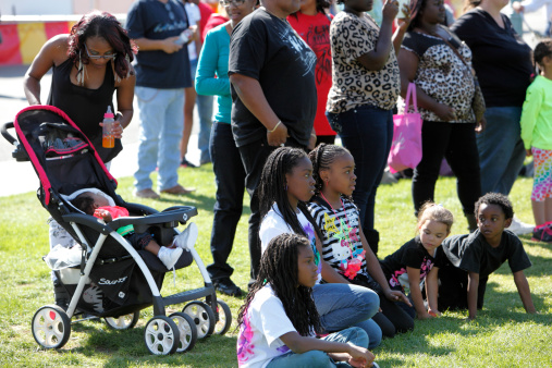Palm Springs,United States- February 23,2013:   Group of Afro American people with children enjoying entertainment at a Black History celebration.  Children are sitting on the lawn watching entertainment which is out of frame. Mother tending baby in stroller.  Black History month is an annual event during the month of February.