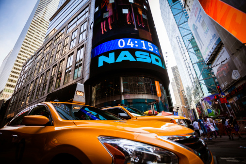 New York City, United States - September 12, 2013: Yellow taxis  under the Nasdaq Sign surrounded by colorful advertisement neon signs and lot of people walking by