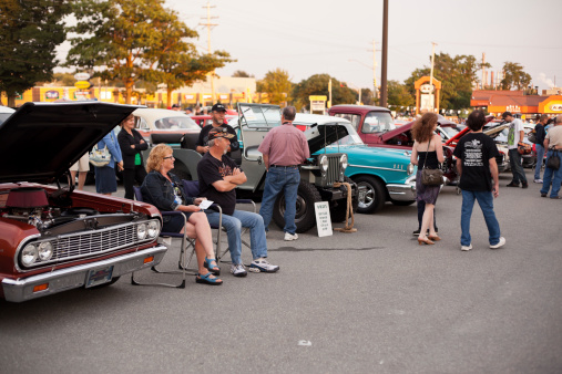 Dartmouth, Nova Scotia Canada - August 23, 2012: A Couple can be seen sitting and talking by a group of people in front of their Chevrolet classic car parked in a parking lot outside in Dartmouth, Nova Scotia, Canada. The cars were parked with other antique cars at a weekly gathering of car enthusiasts which can be seen walking around in the background.