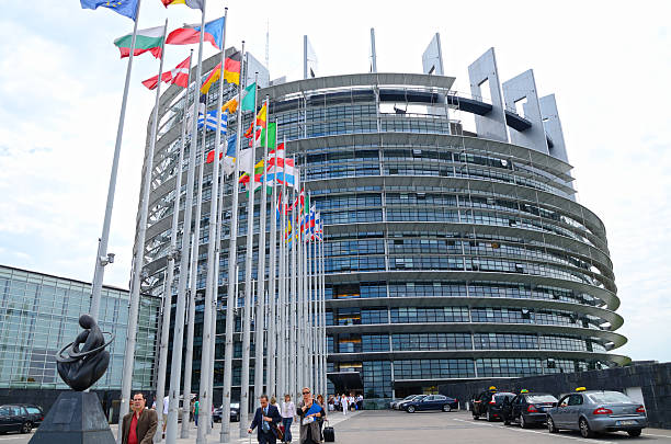 Strasbourg, France - July 5th, 2012: European Parliament wide angle view. Flags of the European Union nations flying in front on tle left. Some cars parked on the right. People going in and leaving the building. Horizontal image