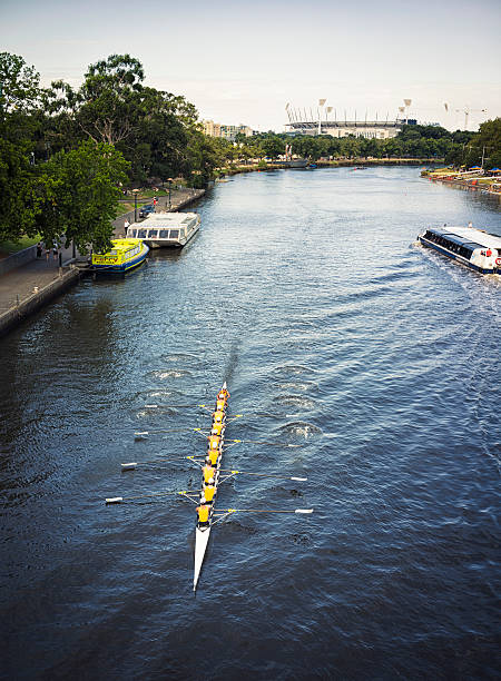 Cambridge, Massachusetts, USA - October 20, 2023: The Head of the Charles Regatta, also known as HOCR, is a rowing head race held on the penultimate complete weekend of October  each year on the Charles River, which separates Boston and Cambridge, Massachusetts United States. It is the largest 3-day regatta in the world, with 11,000 athletes rowing in over 1,900 boats in 61 events. Four women rowers in the foreground. View toward the pedestrian John Weeks Bridge. Harvard University Cambridge campus in the background. Selective focus