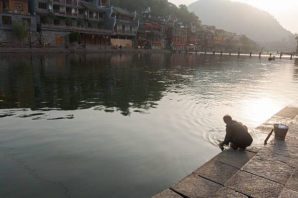 Fenghuang, China - November 4, 2012: Chinese old man washes clothes by the Tuo River in Fenghuang county, Hunan province, China. Fenghuang county is one of the most beautiful town in china and is famous for the old wooden houses projecting over the water along the side of the Tuo River.