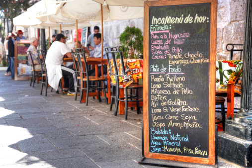 Arequipa, Peru - May 25, 2013: Restaurant menu on blackboard outside street cafes. Men and woman are pictured at the restaurant tables in sunlit cobblestoned street of Arequipa