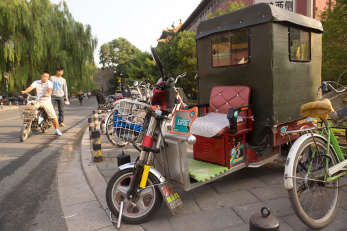 Beijing, China - September 11, 2013: Two cyclists look at a large motorized tricycle parked among bicycles outside the Forbidden City.