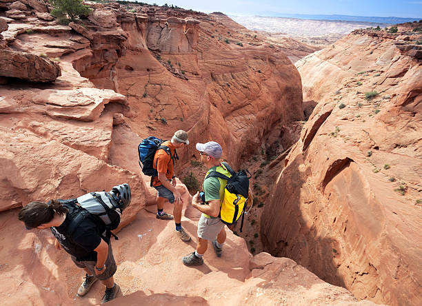 landscape adventure and exploration Escalante, USA- May 21, 2012: Backpacking friends take a look over an enormous cliff leading into the slot canyons of the Escalante.  The unique landscape of Utah is filled with myriad challenges for the adventure minded explorer.  People travel from the world over to experience its inimitable charms. sonoran desert desert badlands mesa stock pictures, royalty-free photos & images