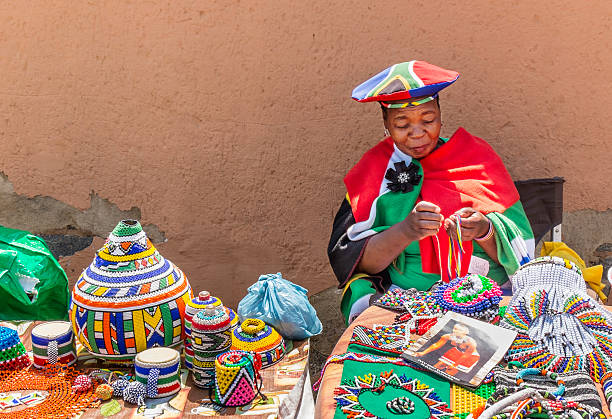 African Zulu lady doing beadwork Johannesburg, South Africa - September, 24th 2013: African zulu lady sitting down doing her beadwork. A display of all her beadworks on the table for sale to tourists along Vilakazi street, in Soweto. soweto stock pictures, royalty-free photos & images