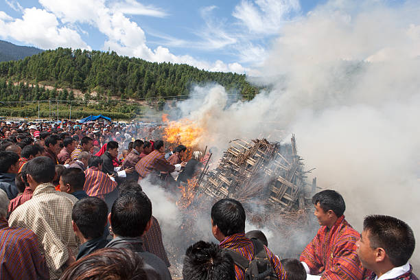 Villaggio di persone saltare attraverso due bruciare haystacks a Thangbi festival - foto stock