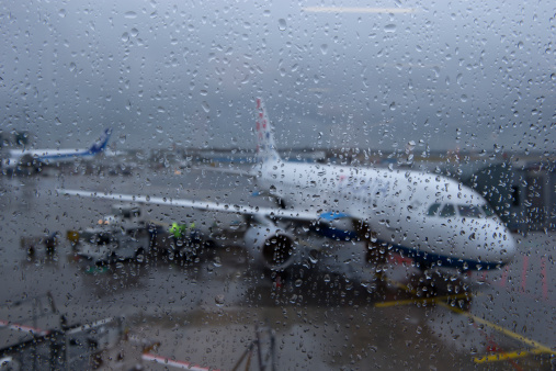 Frankfurt, Germany - July 3, 2013: Rainy Day at Frankfurt Airport, rain drops on window and slight reflections of interior lights. Plane and people out of focus in background, people loading Croatia Airline in background.