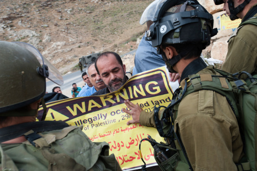 Beit Sahour, Palestinian Territory  - May 12, 2013: Israeli soldiers push back a Palestinian activist holding a sign reading, 