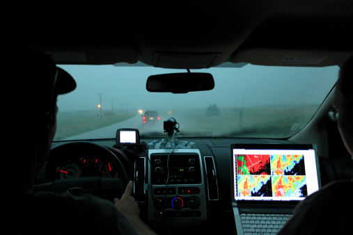 Valentine (NE), USA - May 29, 2010: Two storm chasers drive north along Highway 97 in pursuit of a severe weather event in Nebraska.  They are driving through heavy rain while monitoring various radar data sources on a laptop computer to locate the centre of the storm.  A video camera mounted on the dashboard is used to record the storm and a GPS navigation device assists highway and road selection.