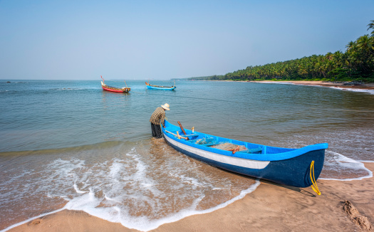 Kannur, India - December 10, 2011: Fisherman prepares to set out on a fishing trip in a small traditional boat along Cherai beach near Thottada village, 10 km south of Kannur, Kerala, India. The shot shows the coconut palms lining the beach along the Malabar coastline.