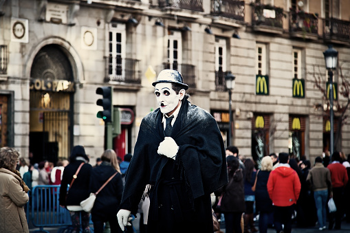 Madrid, Spain - February 9, 2013: Street Performer Dressed as Charlie Chaplin while people walk through a MacDonalds restaurant in Puerta del Sol, Madrid. In this famous square is very typical to see street performers begging.