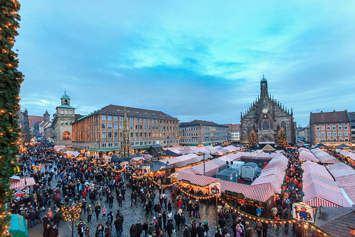 Nuremberg, Germany - December 15, 2012: People crowd the large Hauptplatz, full of the characteristic Christkindlmarkt's stalls covered by awnings in red and white stripes. This Christmas market of Nuremberg is one of the Germany's oldest Christmas fairs. 