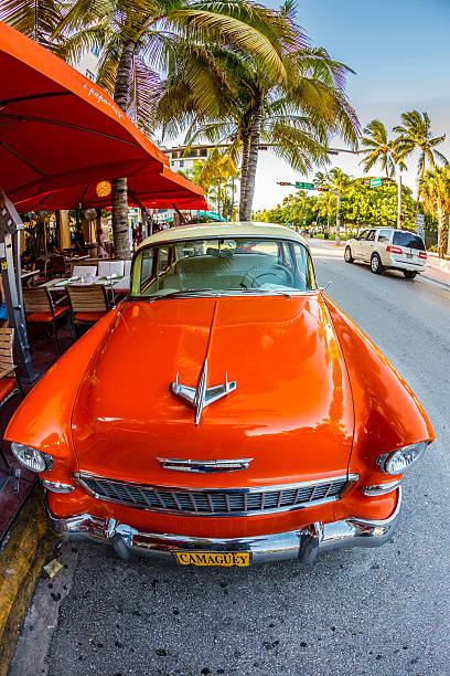 Miami, USA - July 31, 2013: Retro Camaguey Car parked on Ocean Drive in Miami, USA People have lunch in restaurant on foreground.