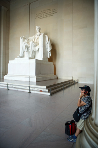 Washington DC, USA - September 7, 2012: Woman leans against a column talking on her mobile phone in front of a marble statue of Abraham Lincoln. Built in 1922, the Lincoln Memorial has been the backdrop for many important speeches, including the historic 