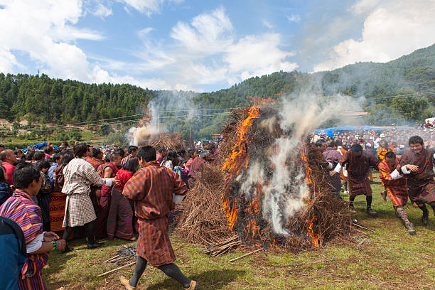 Villaggio di persone saltare attraverso due bruciare haystacks a Thangbi festival - foto stock