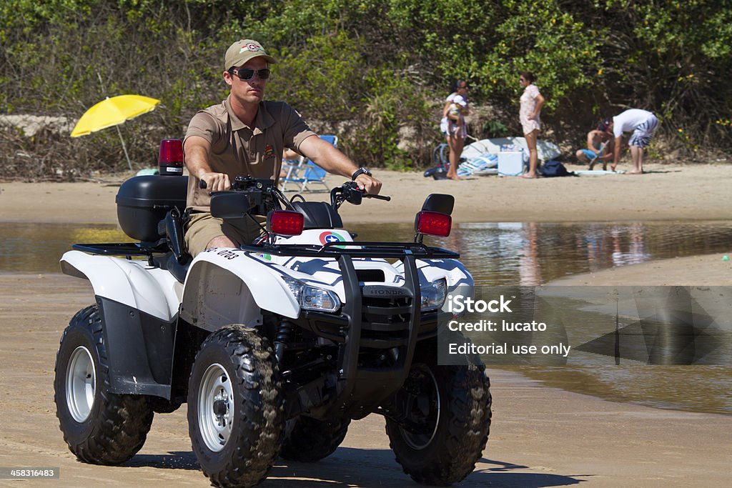 Beach patrolling on quadbike Florianopolis, SC, Brazil - Feb 3, 2012: Beach patrol - A police man on its ATV patroling the beach to keep the beach visitors safe. Police officer hired by the city hall to take care of the public safety. Beach Stock Photo
