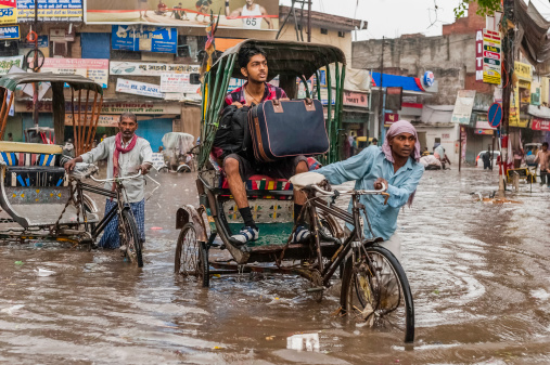 Varanasi, India - August 11, 2011: cycle rickshaws and a passenger with a suitcase try to make headway through a central street in Varanasi despite the heavy monsoon rain and the increasingly risky rising water level as a result of the flash flood.