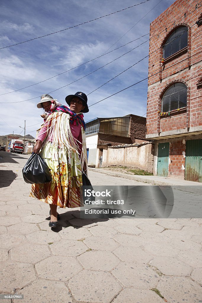 Bolivian woman in traditional dress carrying child on back Copacabana, Bolivia - May 29, 2013: Bolivian woman in traditional dress carrying child on back walking along paved street in Copacabana Adult Stock Photo